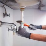 Technician plumber using a wrench to repair a water pipe under the sink. Concept of maintenance, fix water plumbing leaks, replace the kitchen sink drain, cleaning clogged pipes is dirty or rusty.