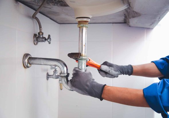 Technician plumber using a wrench to repair a water pipe under the sink. Concept of maintenance, fix water plumbing leaks, replace the kitchen sink drain, cleaning clogged pipes is dirty or rusty.